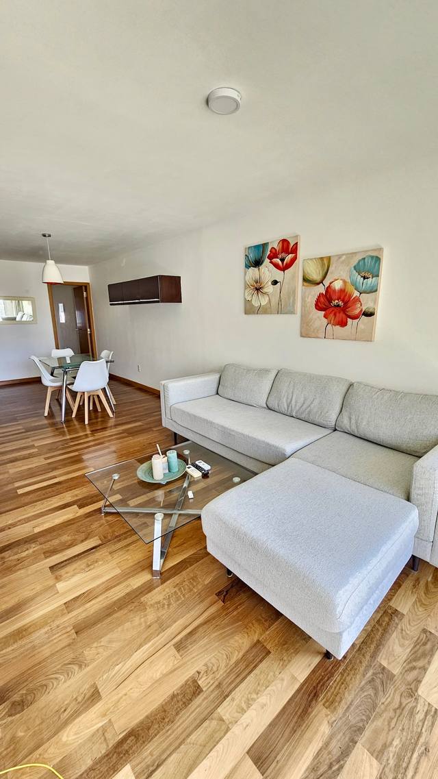 Sala com sofá e quadros, zona de refeições ao fundo