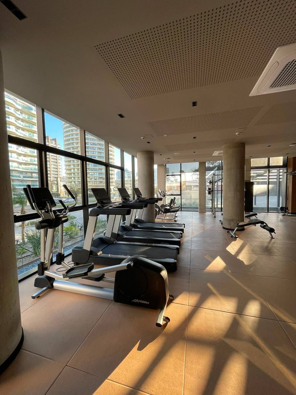 Gimnasio con máquinas de ejercicio y ventanales.